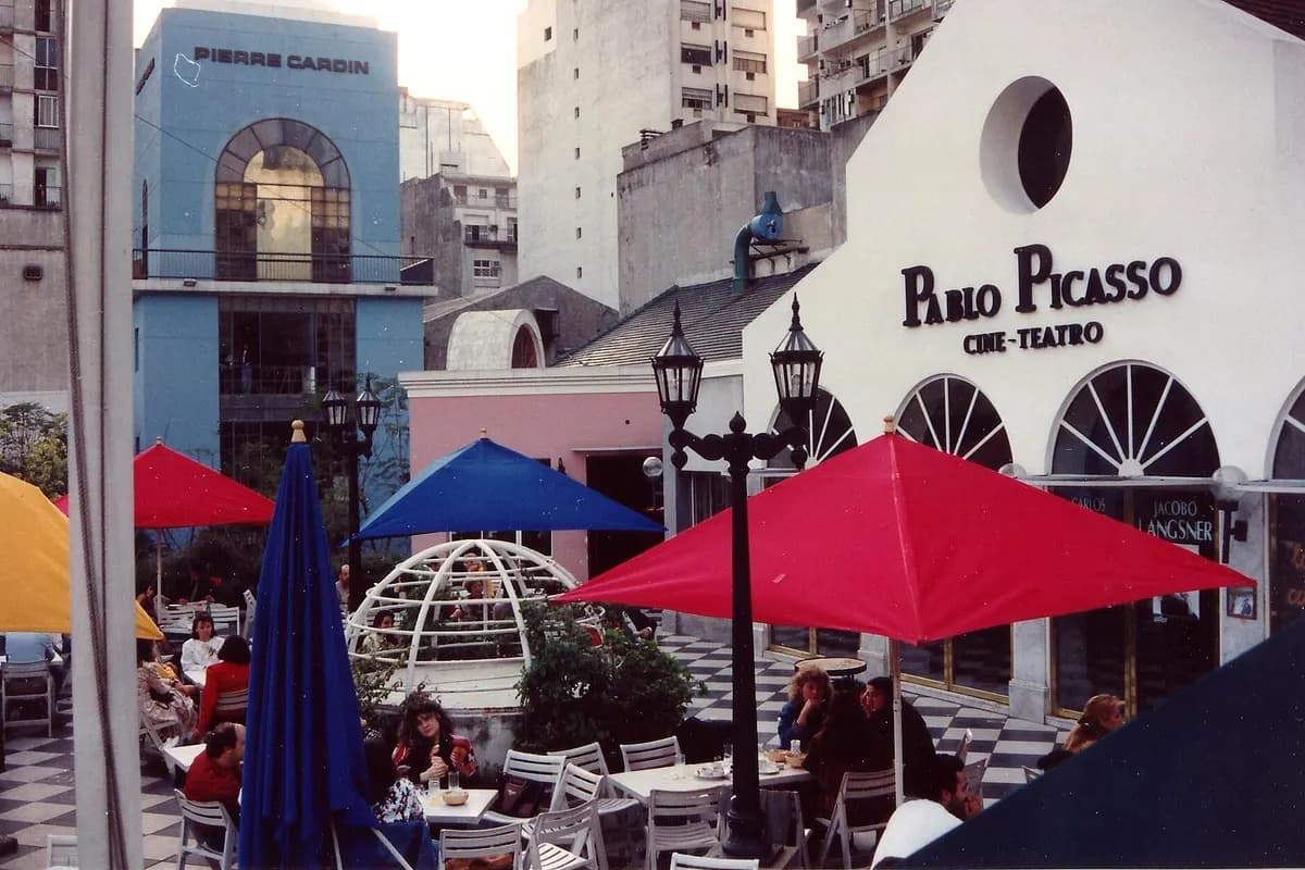 The Pablo Picasso theatre's white gabled front in the Paseo La Plaza courtyard by day, café umbrellas in front